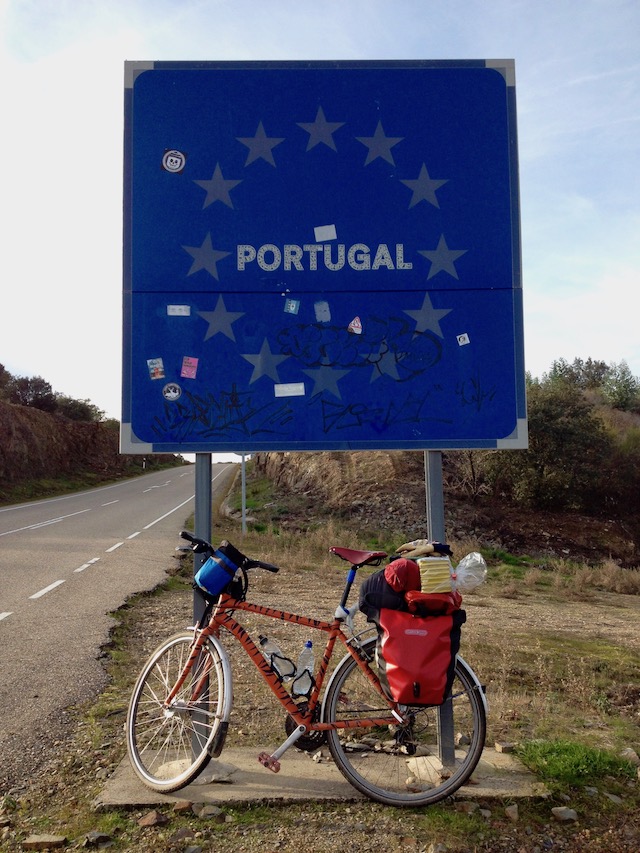 Dans bike, lent against a large blue sign, with the word 'Portugal' in the middle, surrounded by the twelve stars of the European Union (at the border crossing)