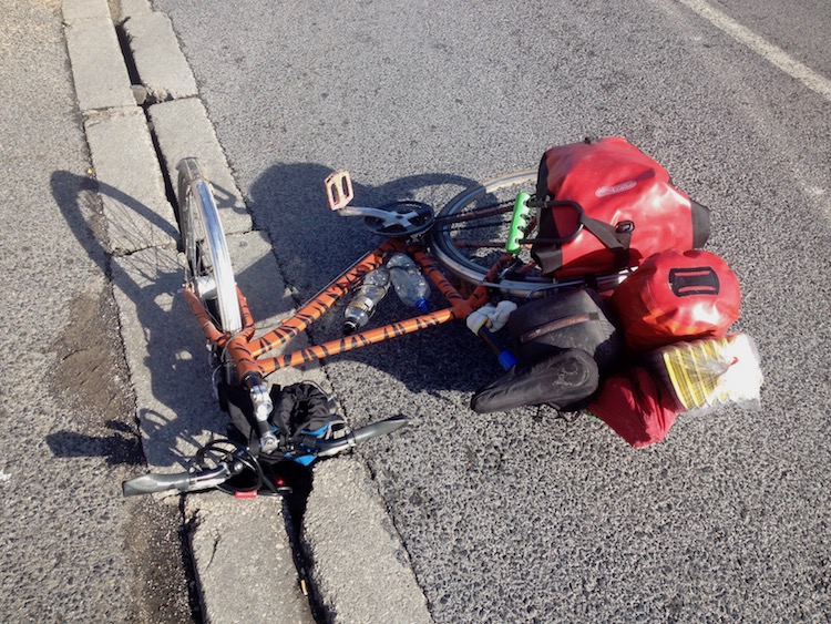 Bike lying on its side on the road, with the front wheel bent downwards, jammed into a drainage slot