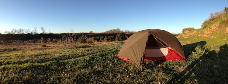 Dan's tent sitting on lush-looking green grass, with clear blue skies and long shadows being cast by the sunset. A small path can be seen running beside the tent.
