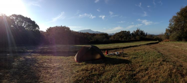 A photo of my tent and bike on top of a hill, with the sun shining and a mountain in the background (wild camping)