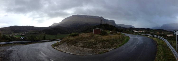 Panoramic view of wet road in Cantabrian Mountains, Spain, with low grey clouds surrounding mountain peaks in the background
