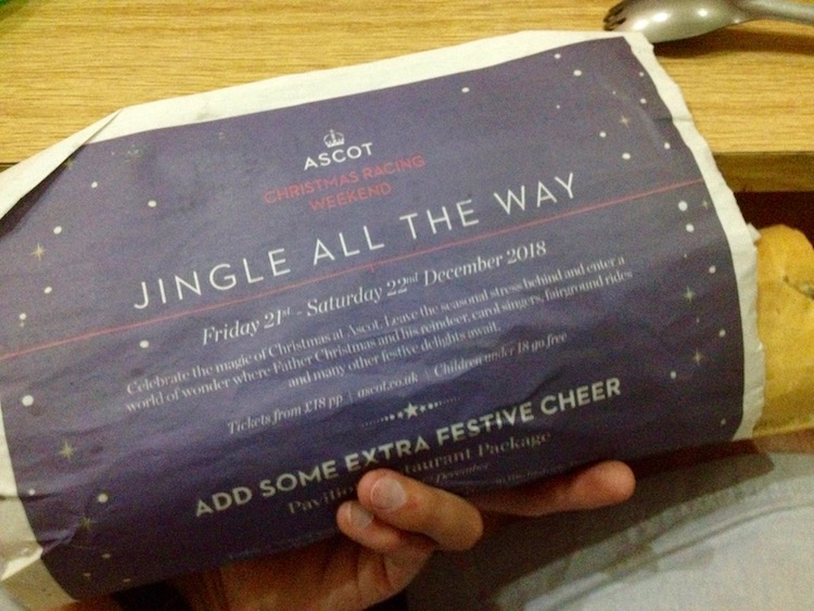 A sandwich held in Dan's hand. It is wrapped in a page of a newspaper, and the sentences, 'Jingle all the way,' and, 'Add some extra festive cheer,' can be seen.