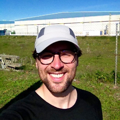 Selfy showing Dan grinning goofily, wearing a cheap, light-grey cap, at the roadside.