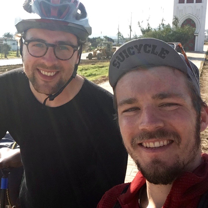 Dan and Nico smiling for a selfy, both wearing helmets, on their bikes.