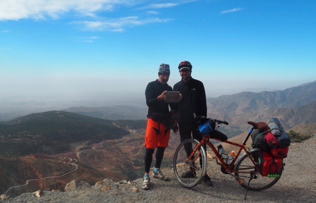 Dan standing with his bike and another man, looking at a tablet computer, with the huge view in the background.