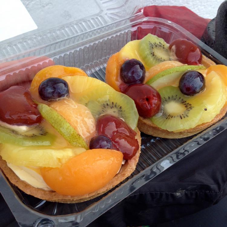 Two large fruit pastries (containing kiwi, grapes, cherry, orange, apricot and custard) in a plastic container.