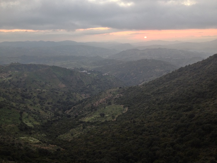 Long distance view over many mountain peaks, with the sun large and almost disappearing behind the horizon.