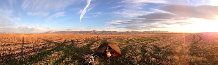 An ocean of flat grass, with mountains on the horizon and Dans tent set up in the foreground (facing the camera), the sun rising from one side (panoramic shot, wild camping in northern Spain)