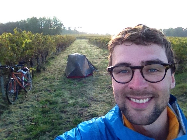 A selfy of Dan on a Bordeaux vineyard, with his bike and tent in the background (wild camping).